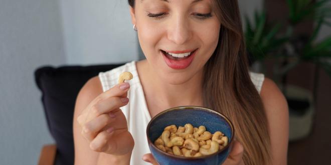 a young woman smiling while eating raw cashews